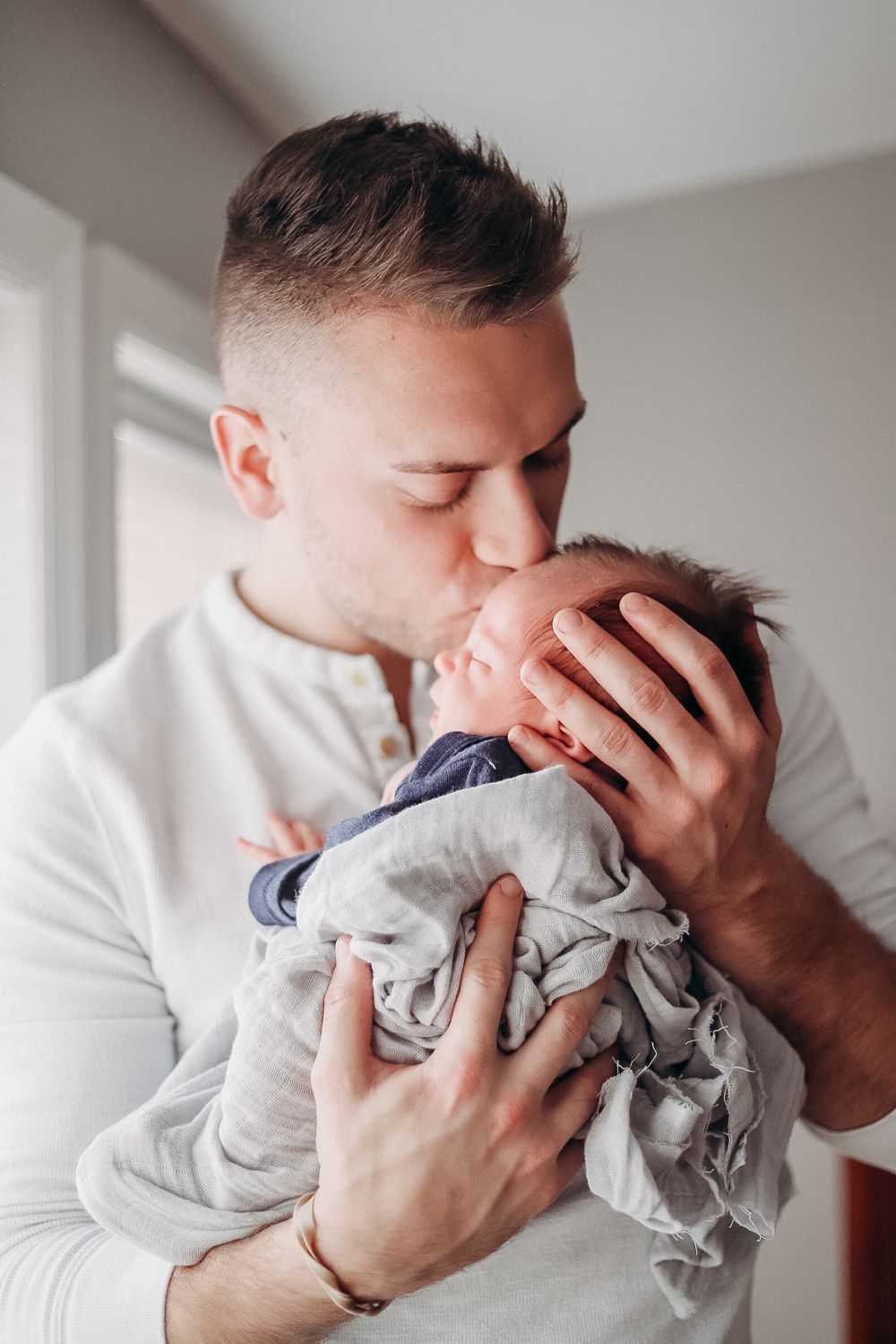 Emotional series showing parent holding and kissing newborn baby in white room.