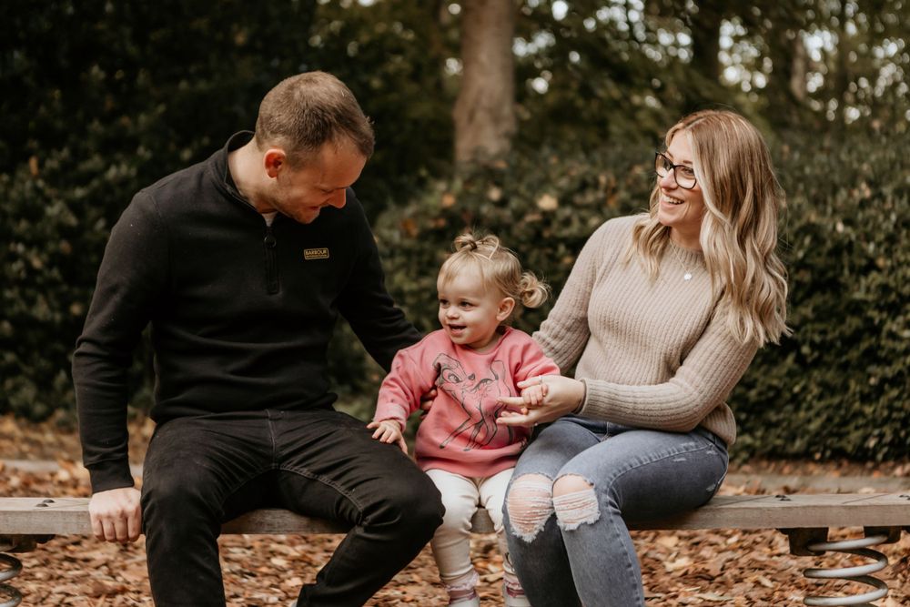 Casual family moment captured on a wooden bench surrounded by fall leaves.