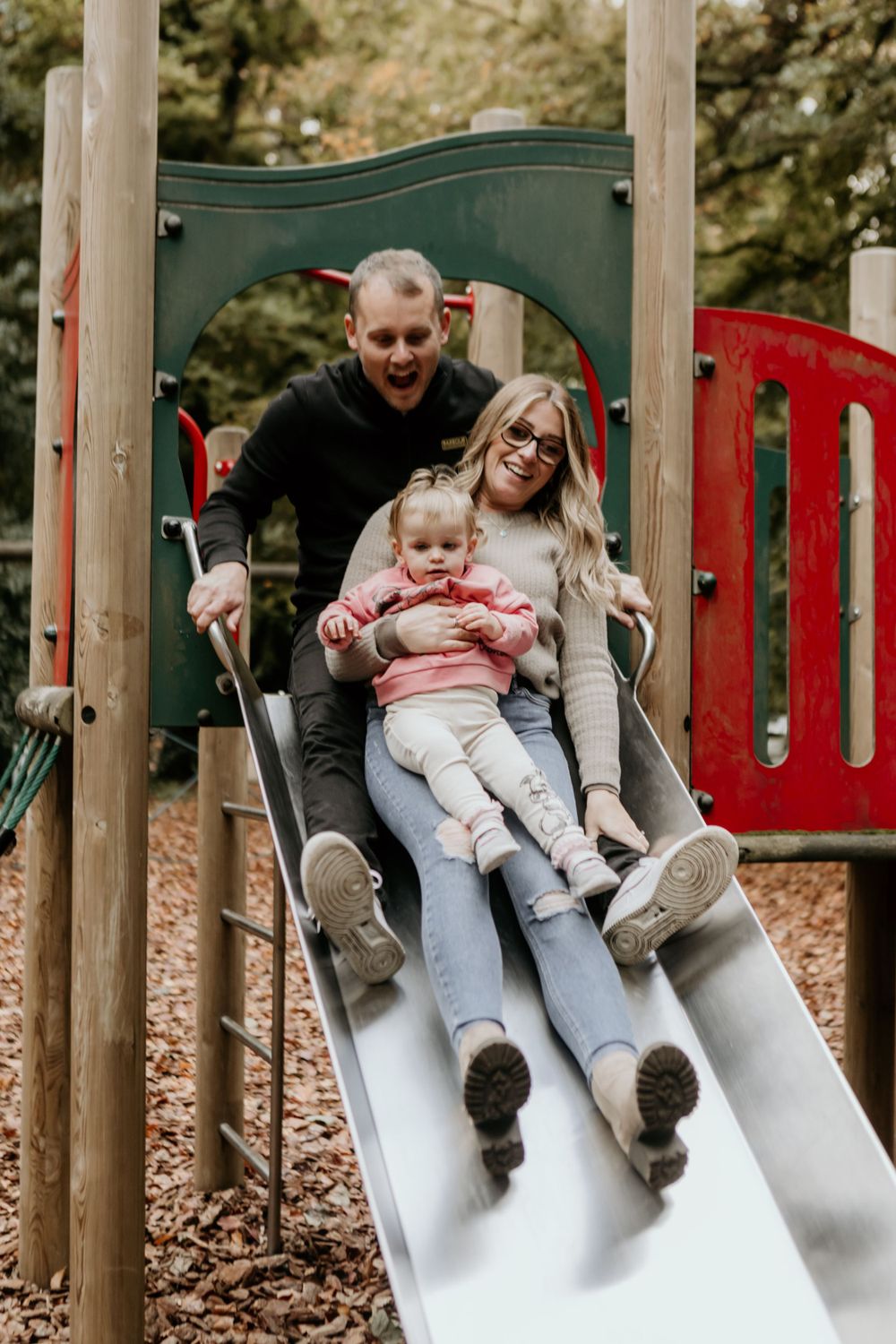 Playful family moment on a playground slide with autumn leaves scattered on the ground.