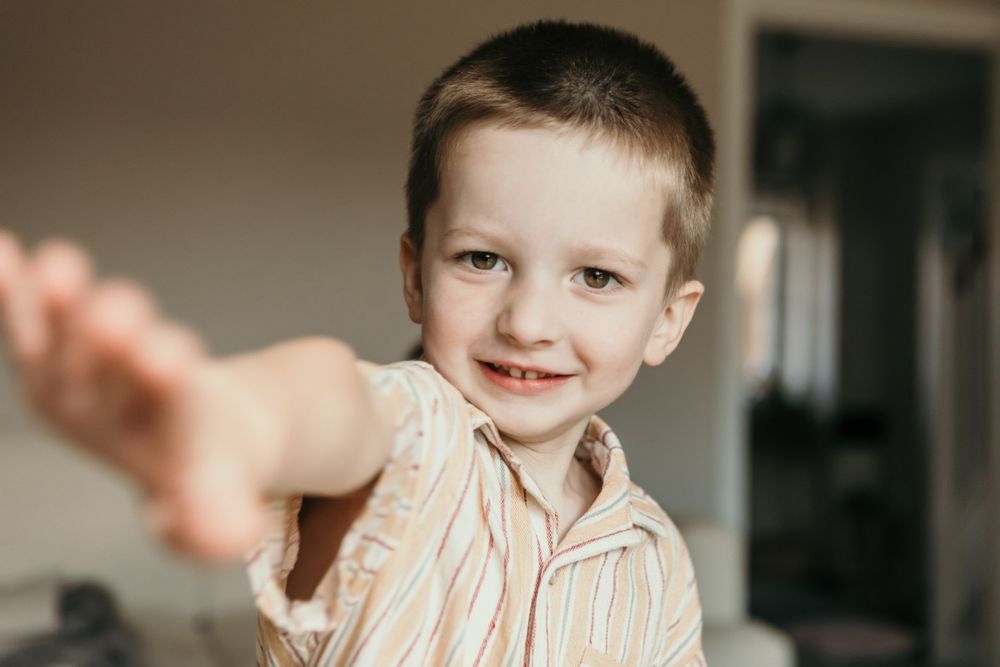 A child in striped pajamas smiling and reaching toward the camera.