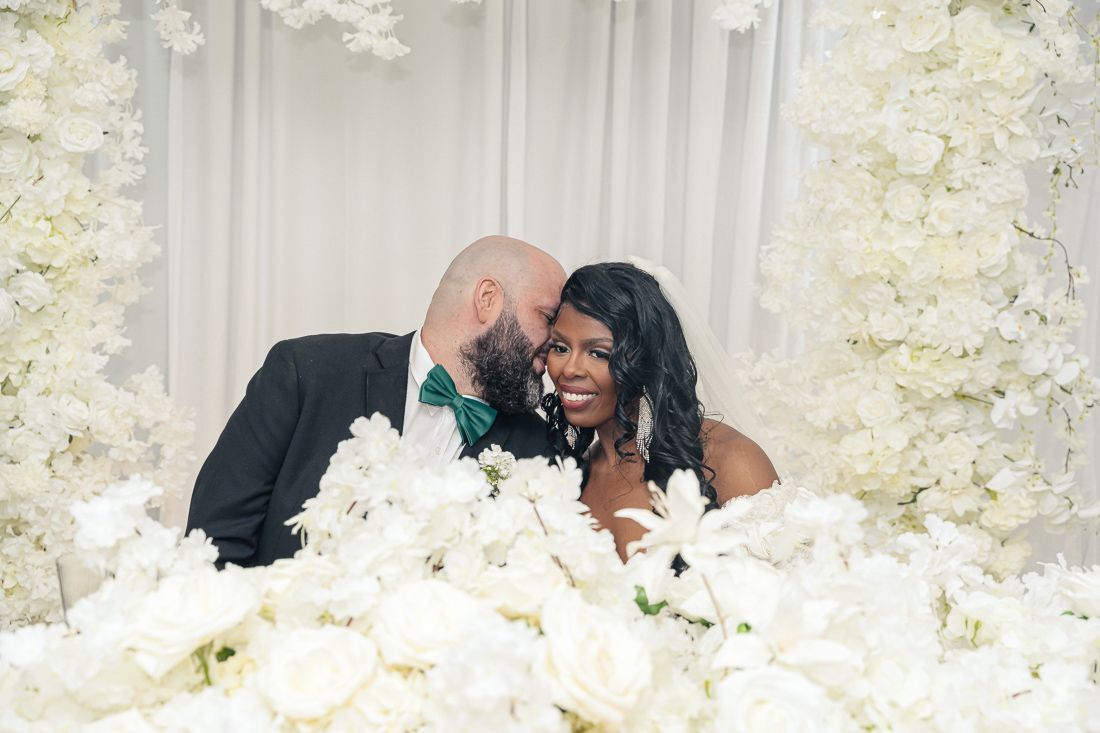 Newlyweds share an intimate moment surrounded by white floral decorations at their wedding celebration.