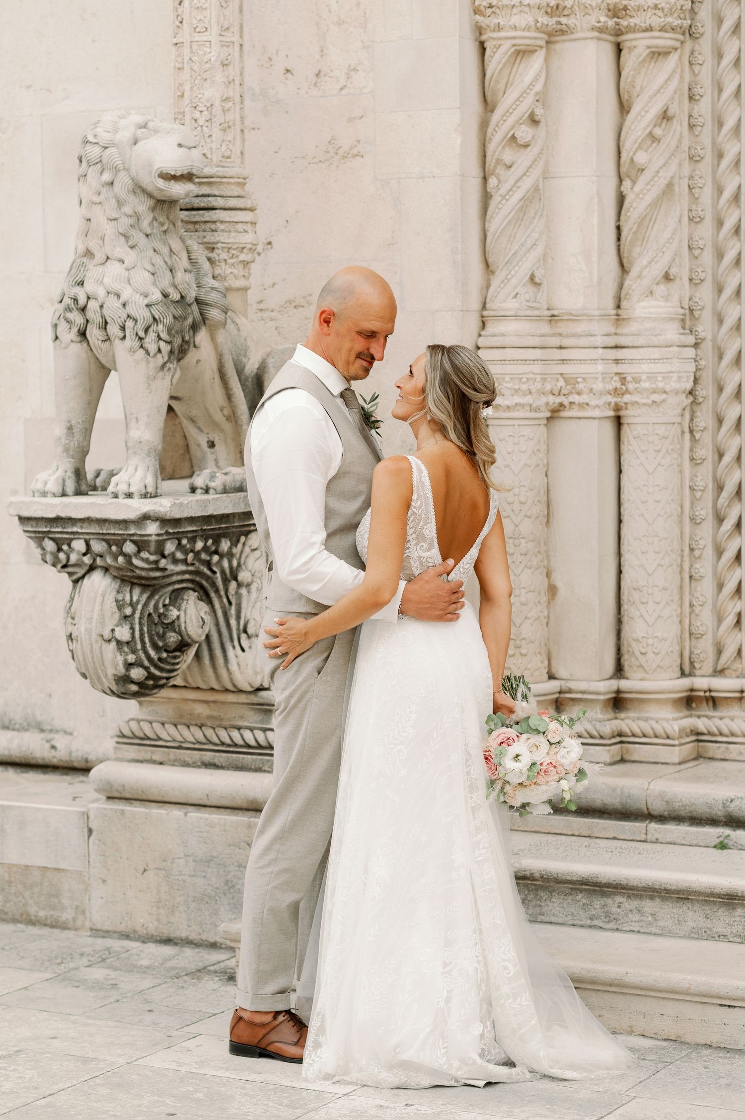 Wedding portrait by architectural columns and stone lion statue with delicate bouquet.