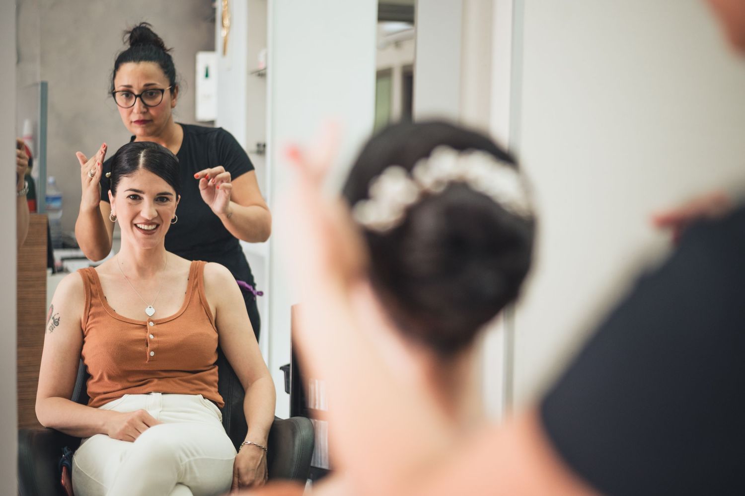 A hairstyling session captured in a salon mirror reflection.