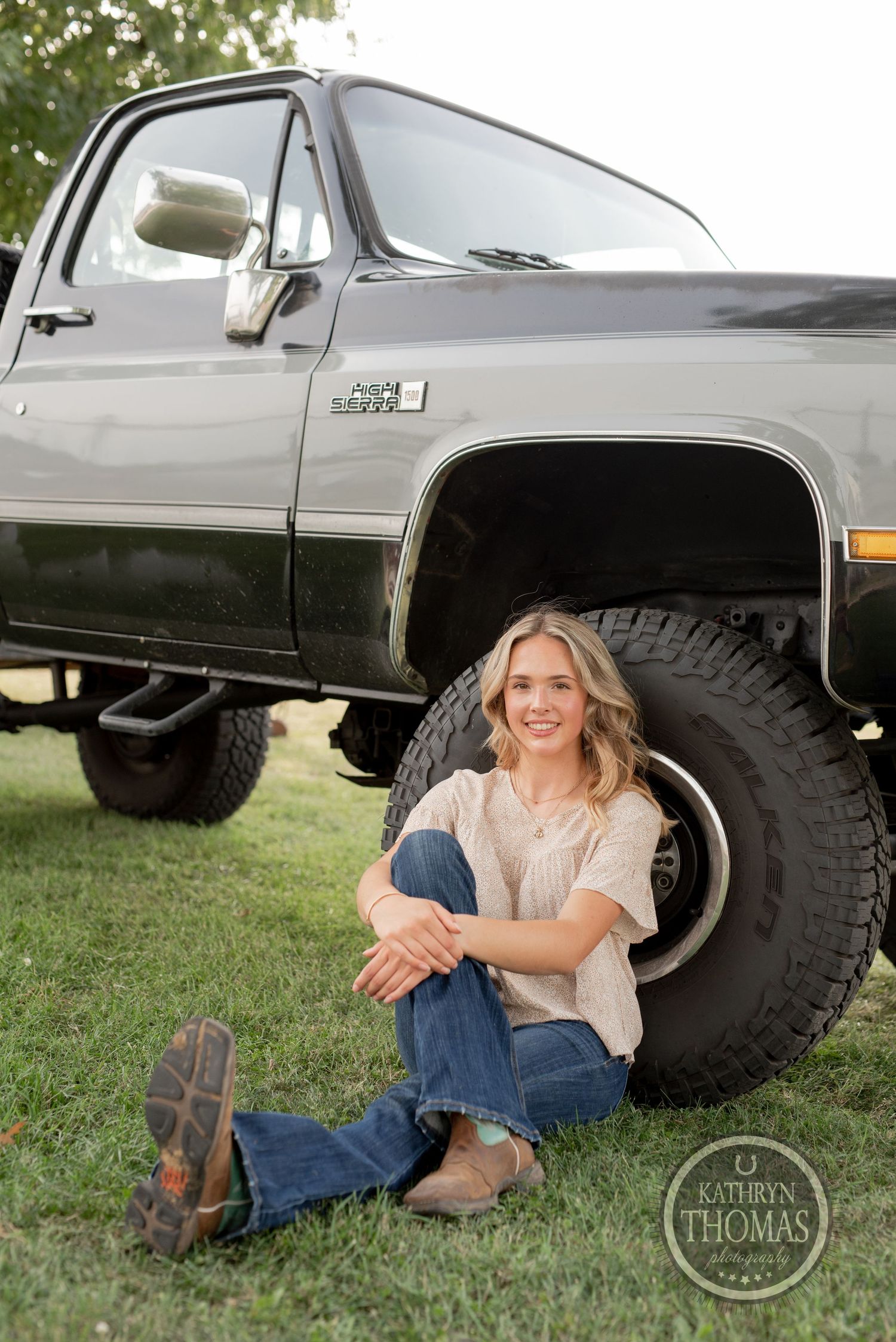 Someone sits casually by the large tire of a lifted vintage pickup truck.