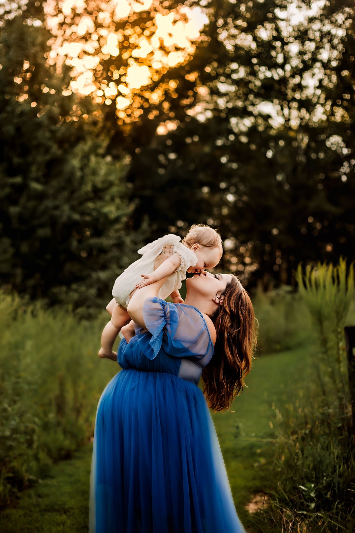 A joyful moment at sunset with a woman in blue dress lifting a small child wearing white.
