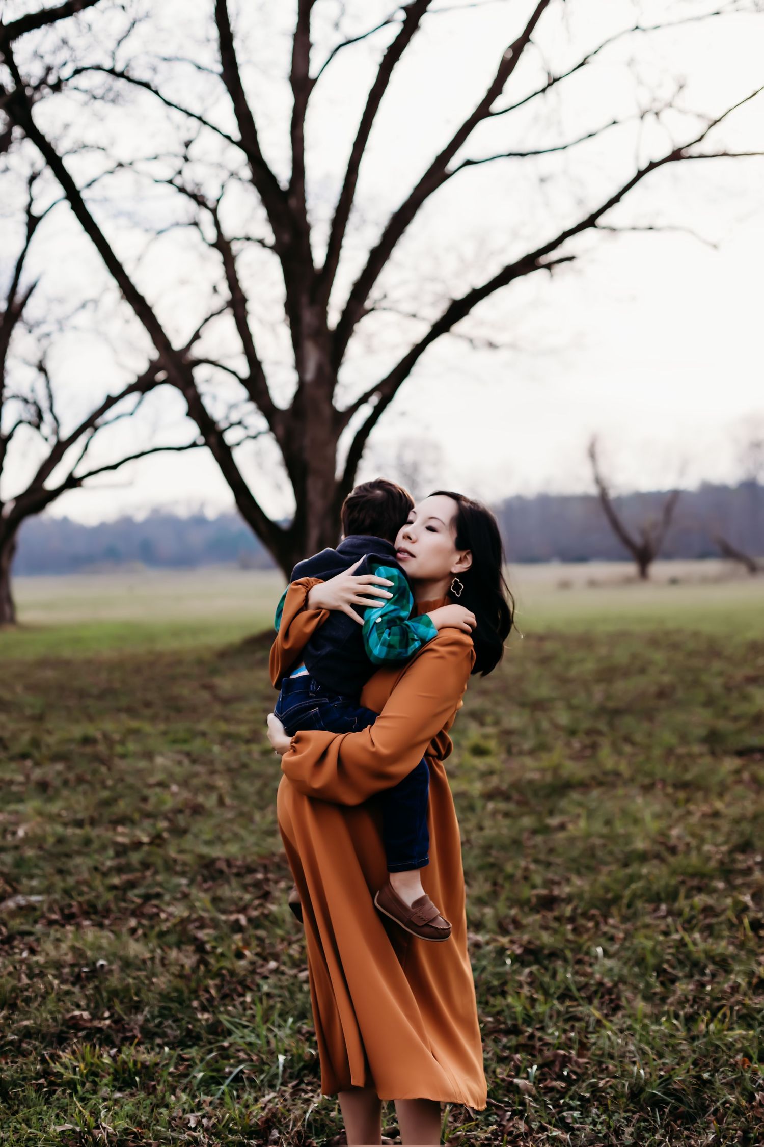 Autumn portrait of parent and child embracing under bare trees in field.