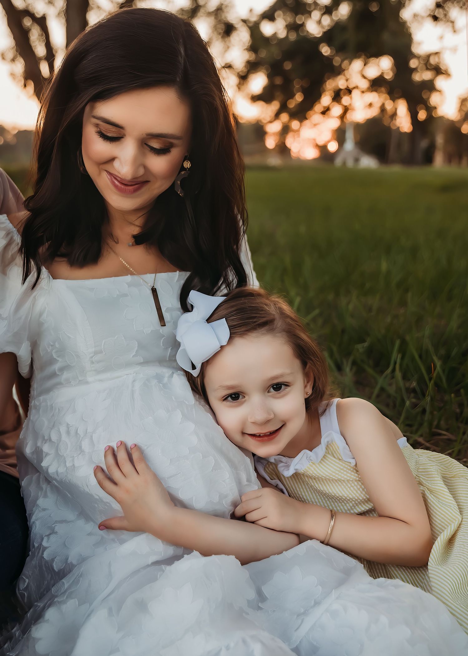 A sweet moment between a pregnant woman in white and a child hugging her baby bump.
