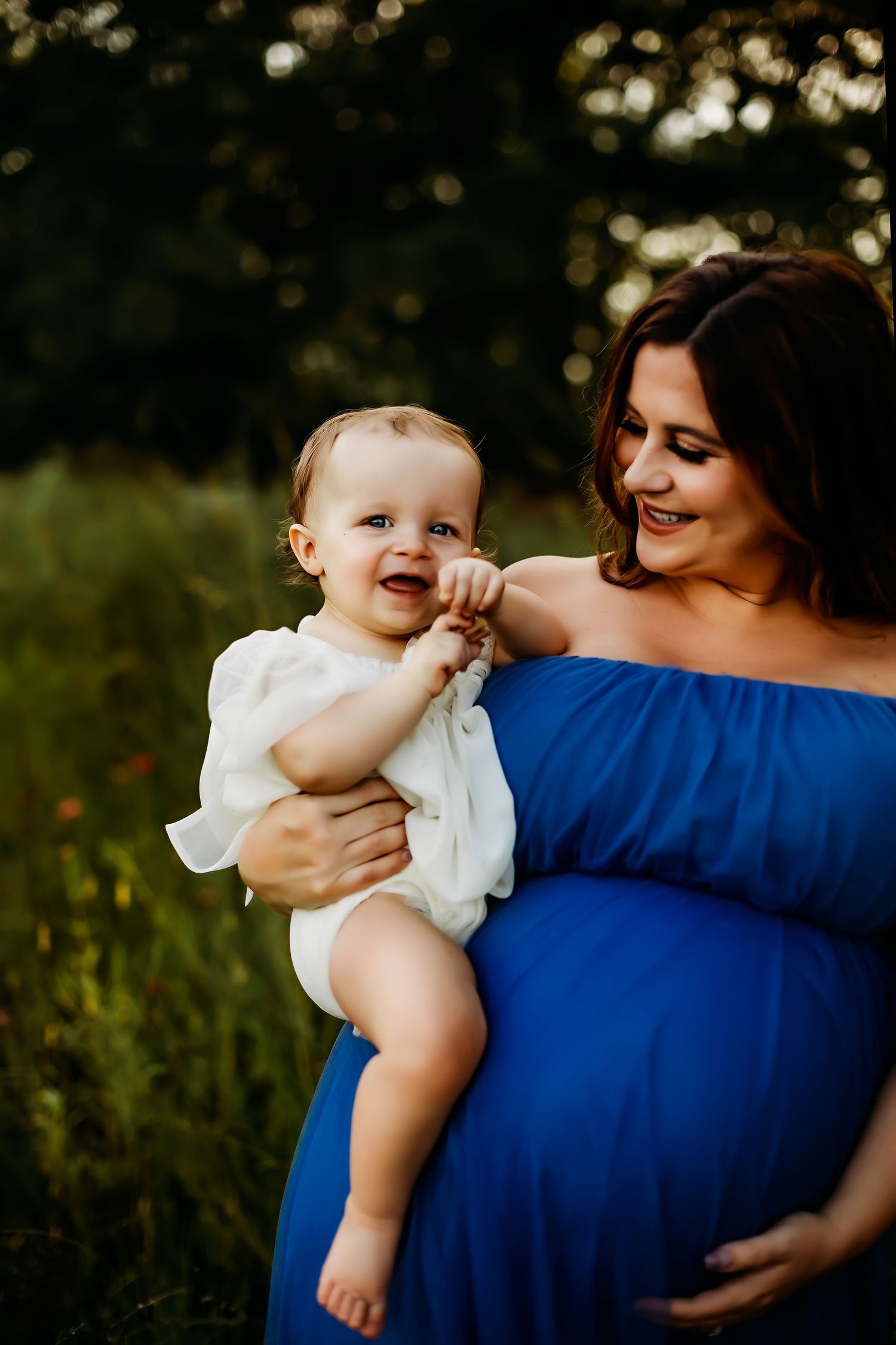 A heartwarming maternal moment captured between a baby in white and a woman in a blue dress outdoors.
