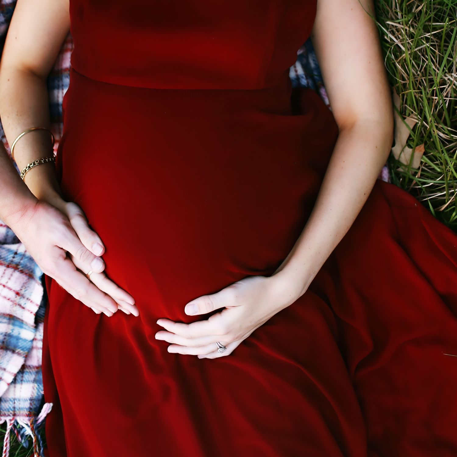 Hands rest gently on a red dress against grass background.