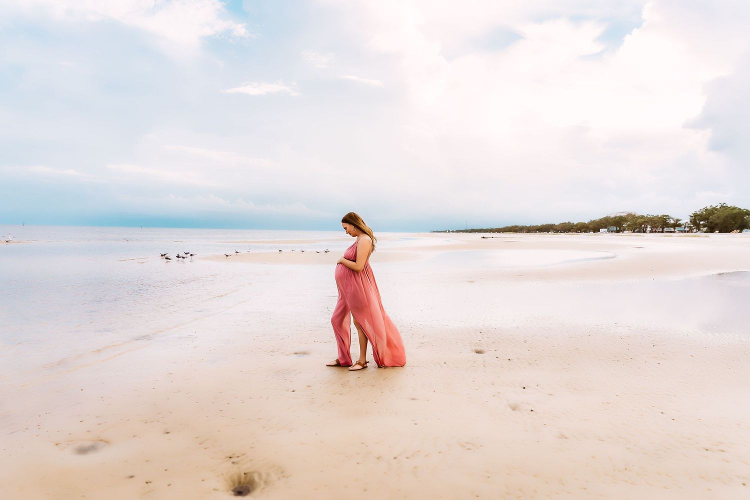 A flowing coral maxi dress billows in the wind on a serene white sand beach with ocean views.