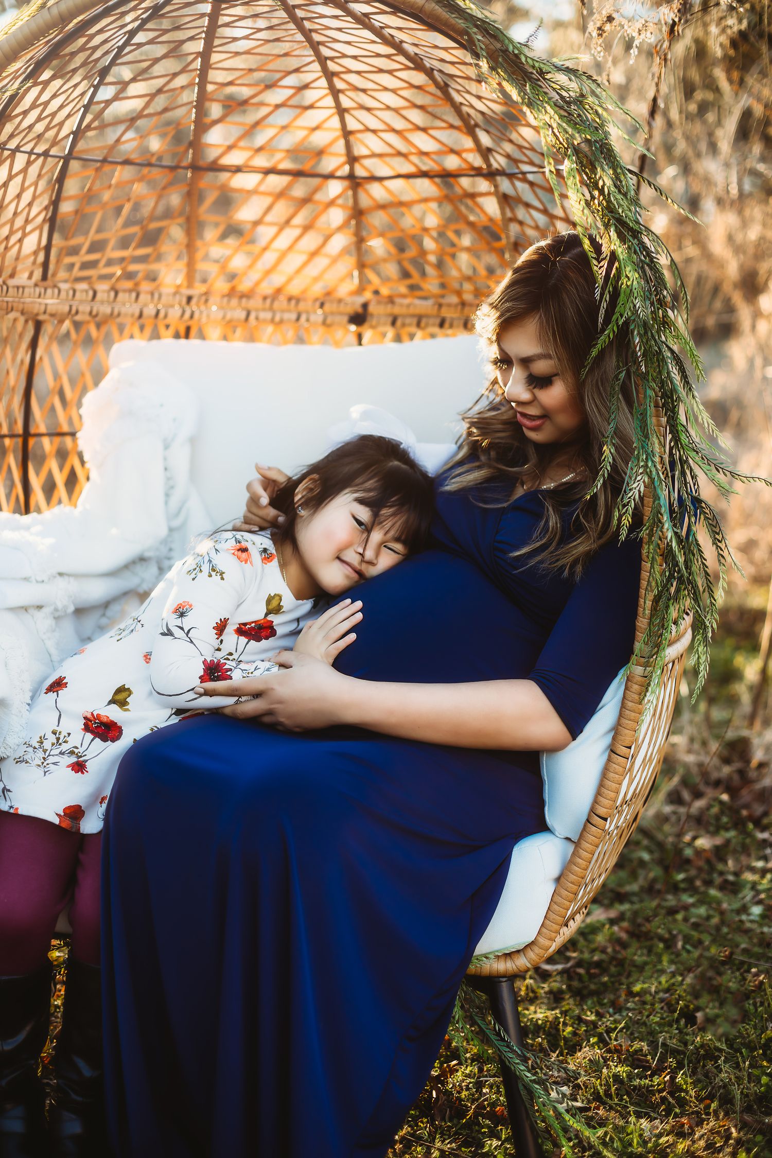 Mother and child share quiet moment together in woven egg chair outdoors at sunset.
