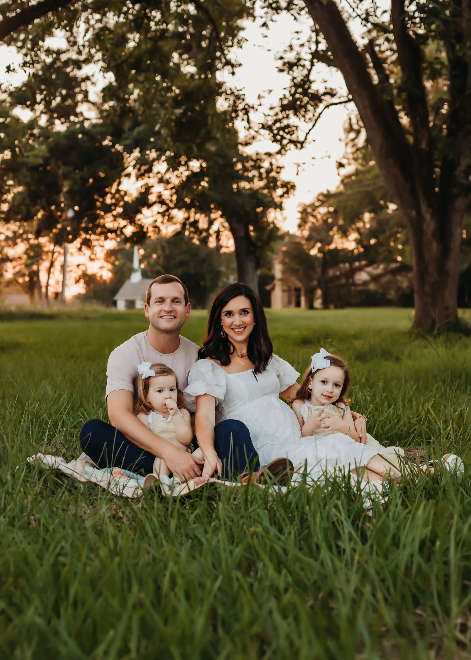 A family sitting together on a blanket in a grassy field during sunset.