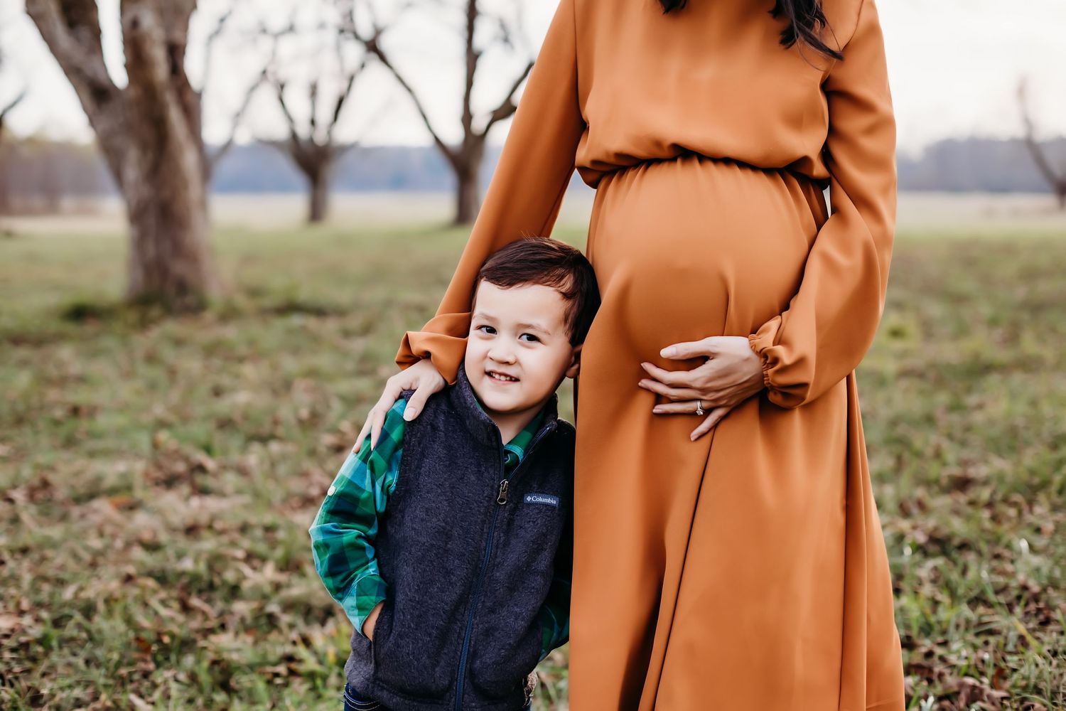 Maternity photo with young child in navy vest next to rust-colored dress.