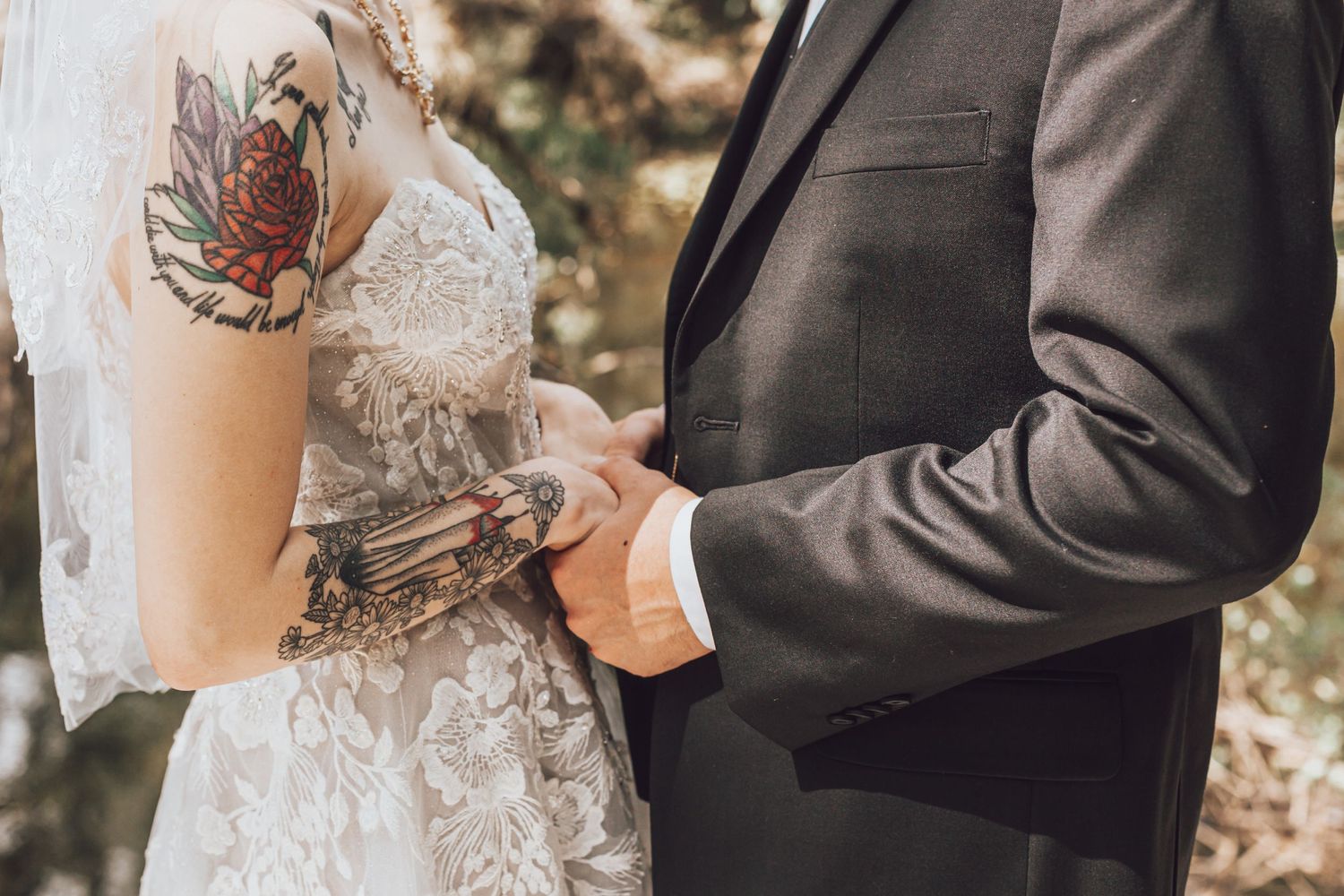Close up of a couple holding hands showing intricate tattoo details and wedding attire.