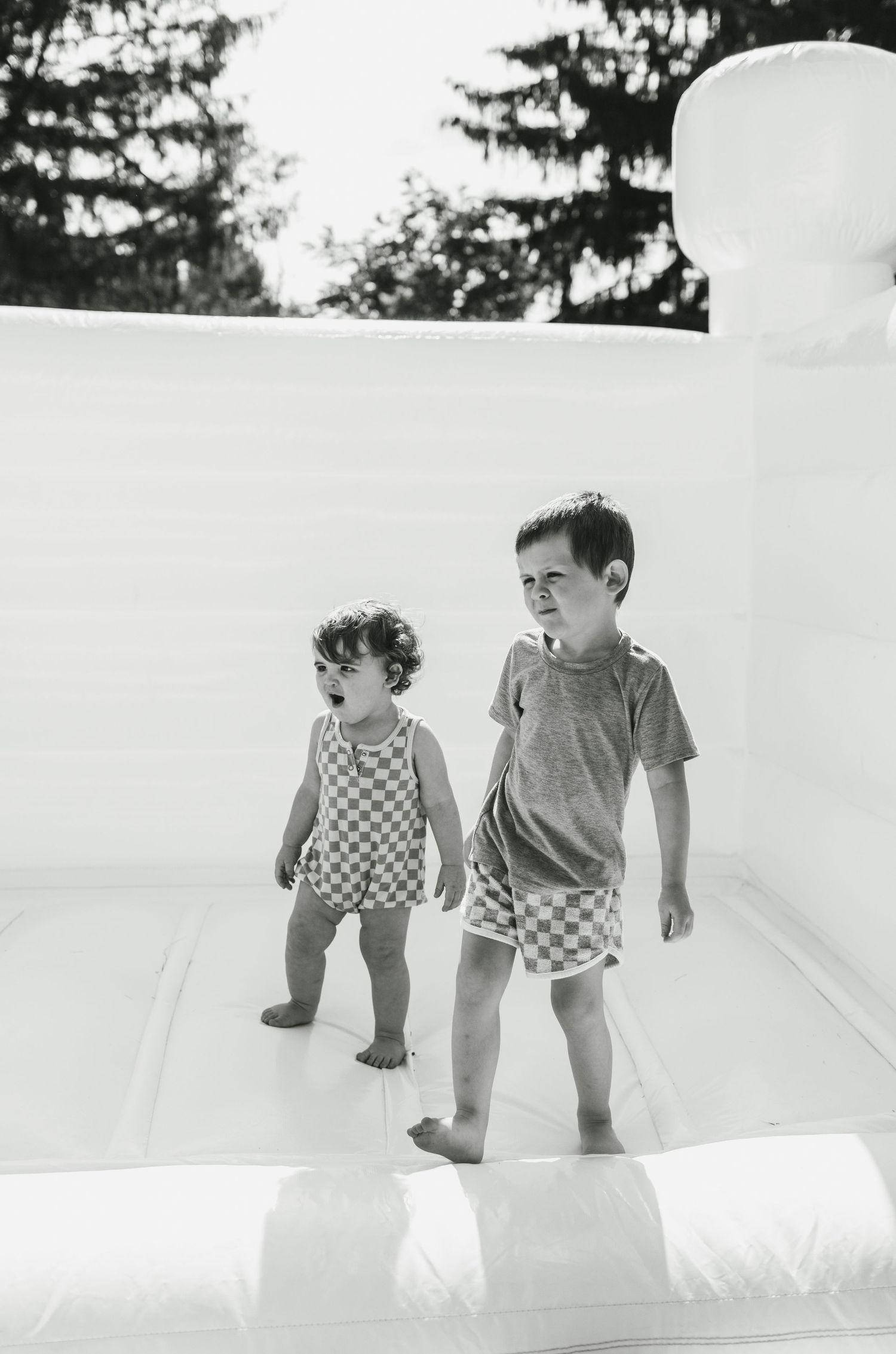 Two young children playing on a white bouncy castle in black and white photography.