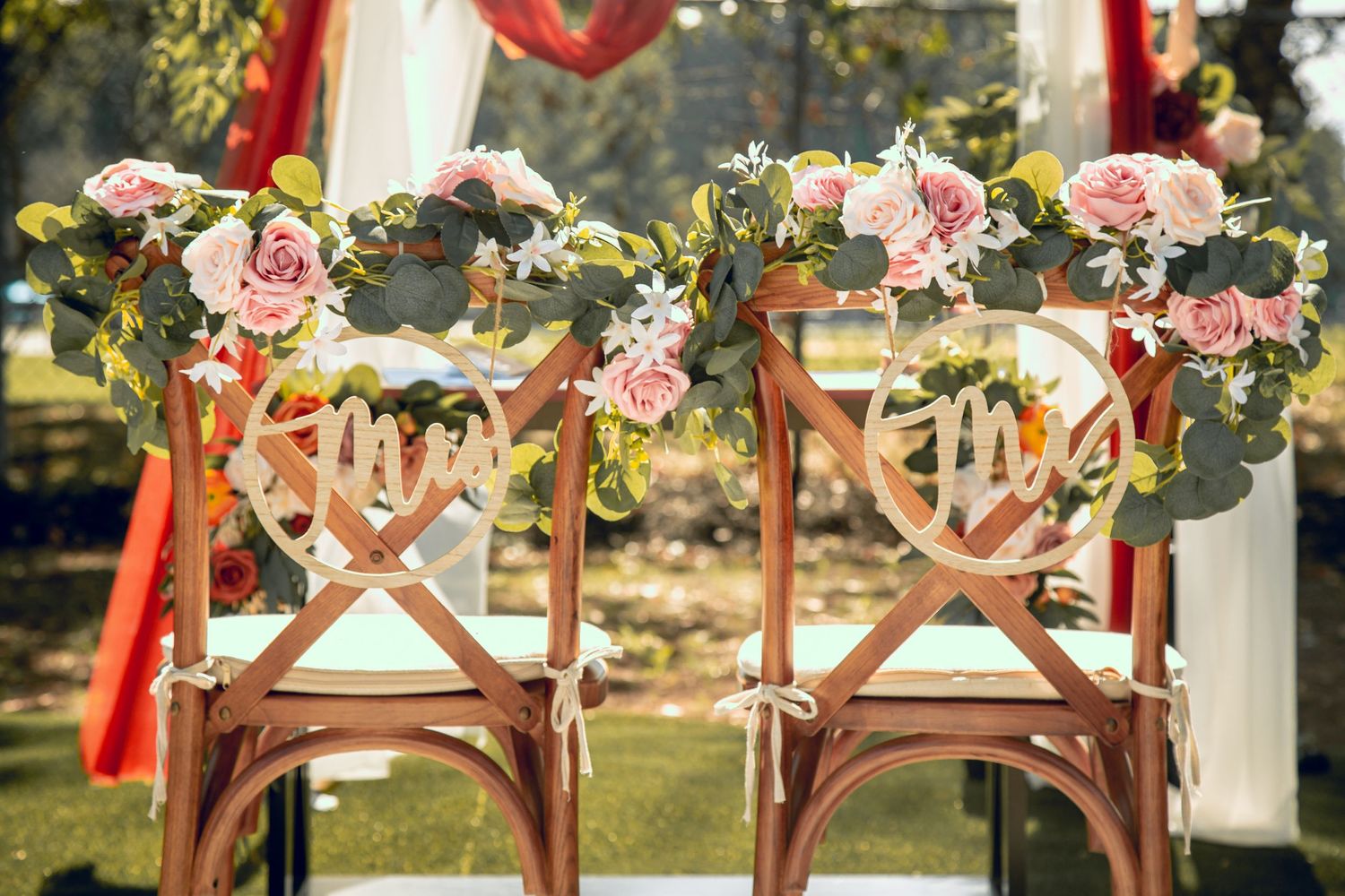 Wedding chairs decorated with pink floral garlands and heart decorations in outdoor setting.
