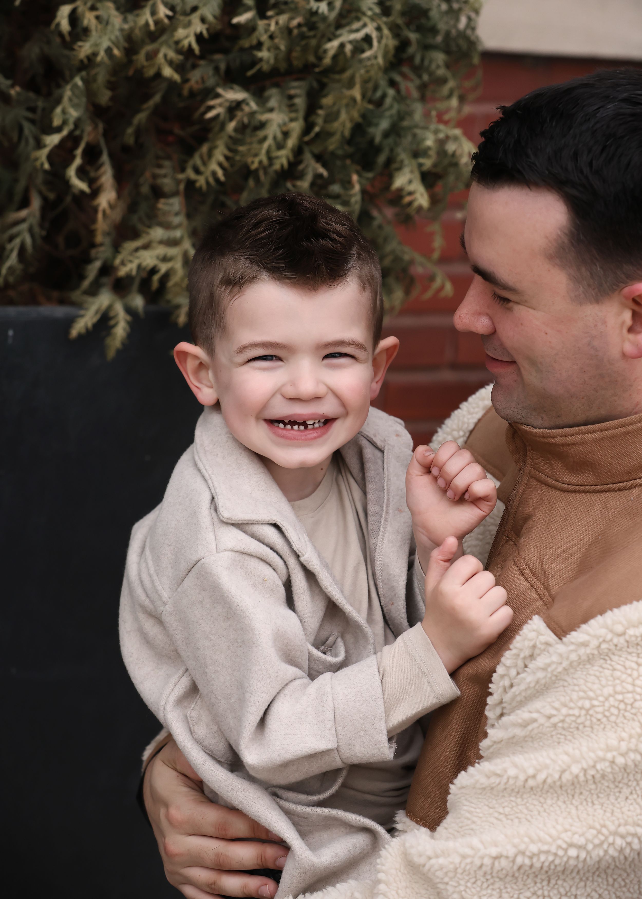 Candid lifestyle portraits showing genuine laughter and connection against brick wall.