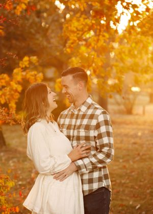 A couple embraces in a romantic autumn setting with golden leaves and sunlight creating a warm atmosphere.