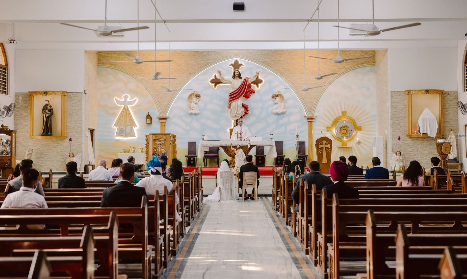 Wide panoramic view of a church interior with rows of wooden pews and religious artwork.
