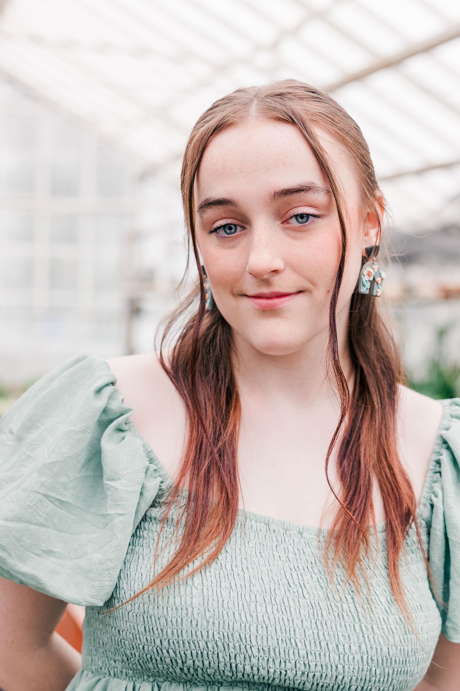 Woman in mint green smocked dress with puff sleeves poses in a greenhouse.
