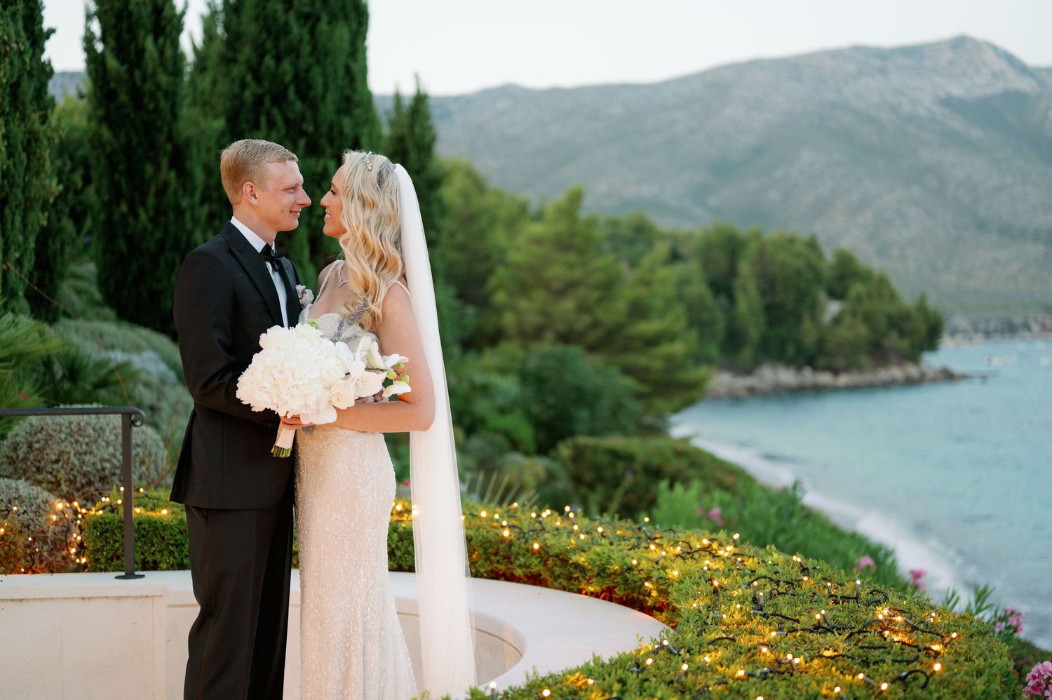 Scenic coastal wedding portrait with mountain and sea views in background.