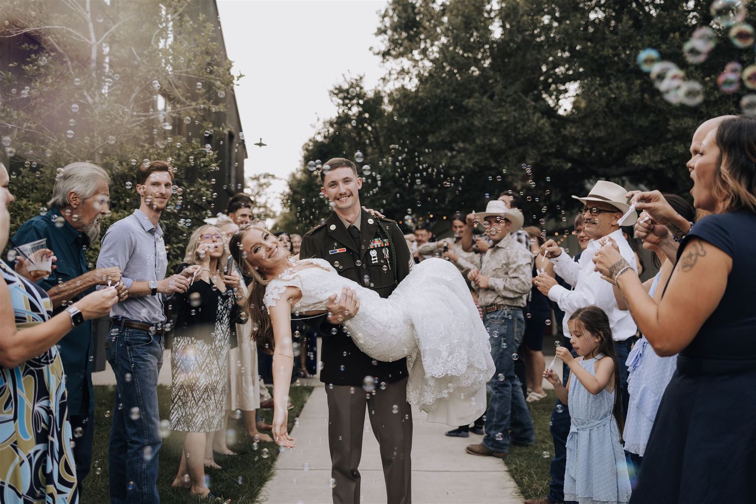 A couple dips in celebration while guests blow bubbles during an outdoor wedding exit.
