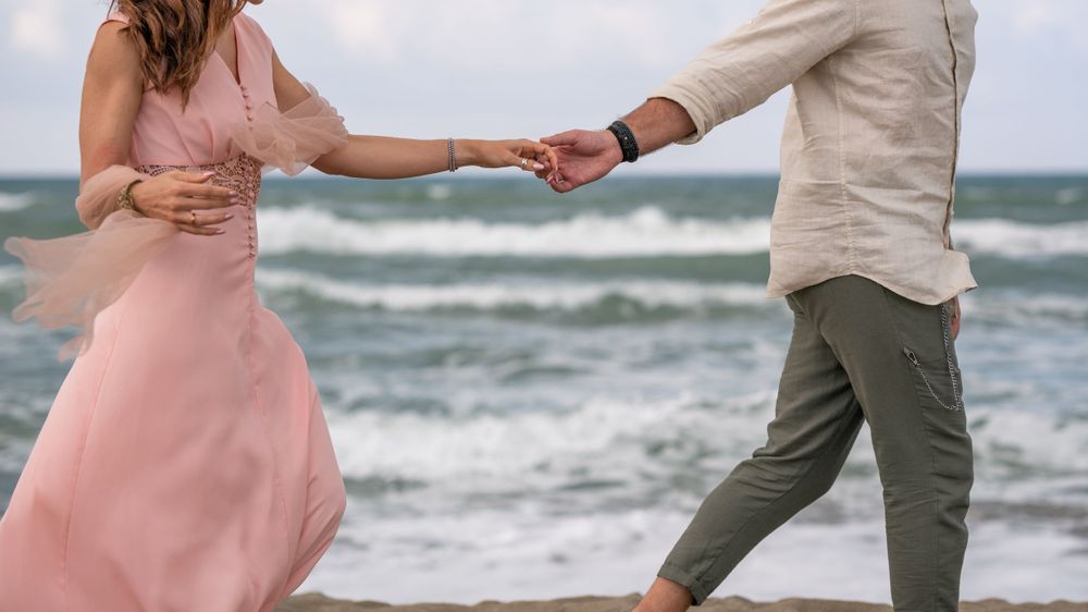 Two people dancing barefoot on beach with waves splashing in background.