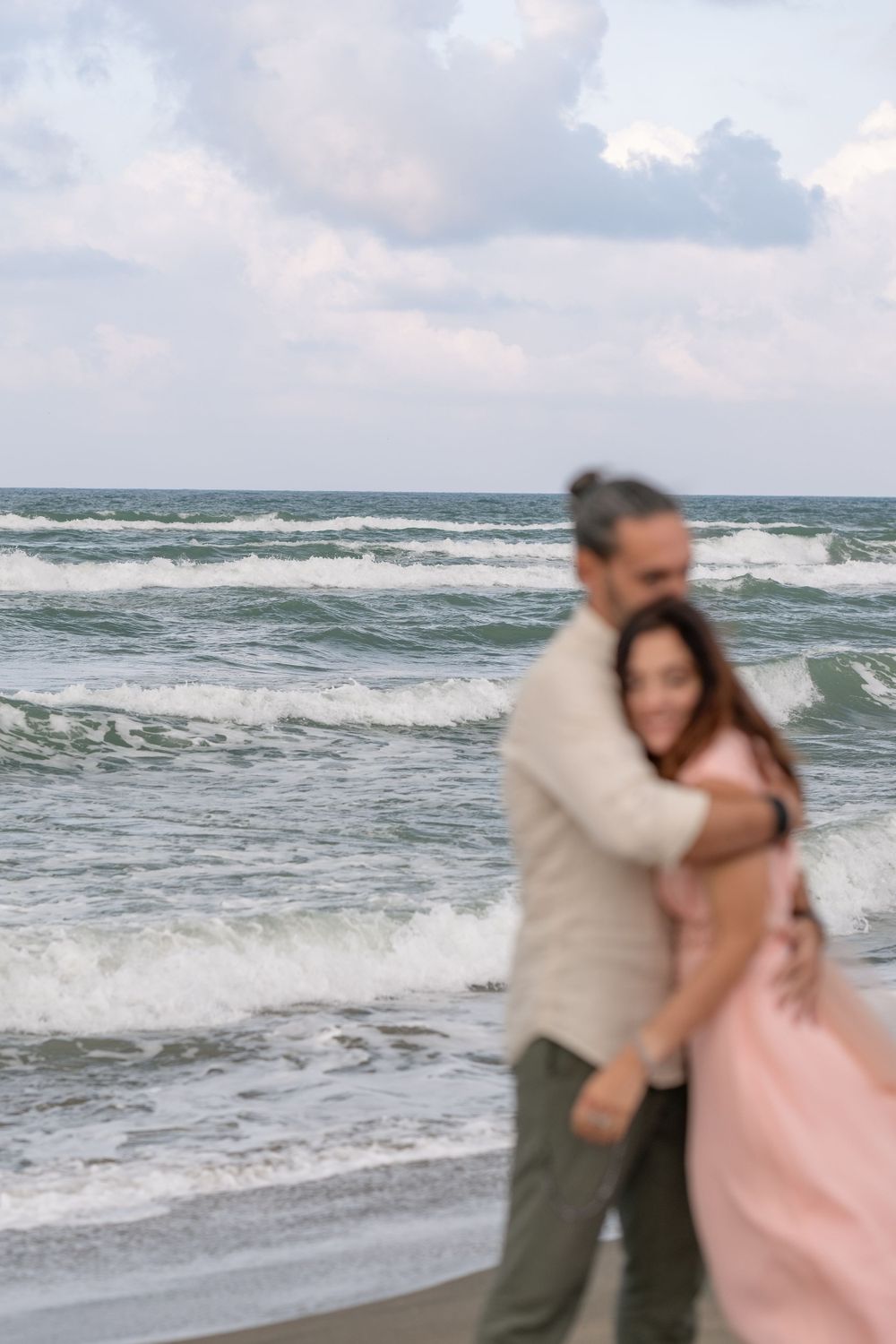 Romantic beach moment with waves crashing and cloudy sky backdrop.