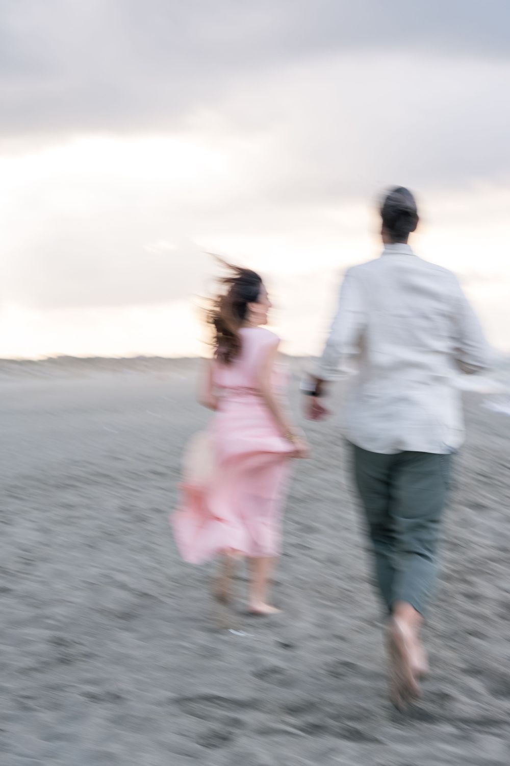 Motion-blurred photo of a couple running together on sandy beach at dusk.