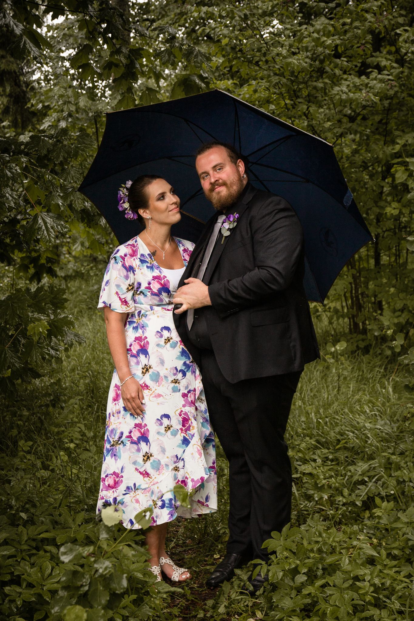 Woman and man standing underneath an umbrella in the woods.