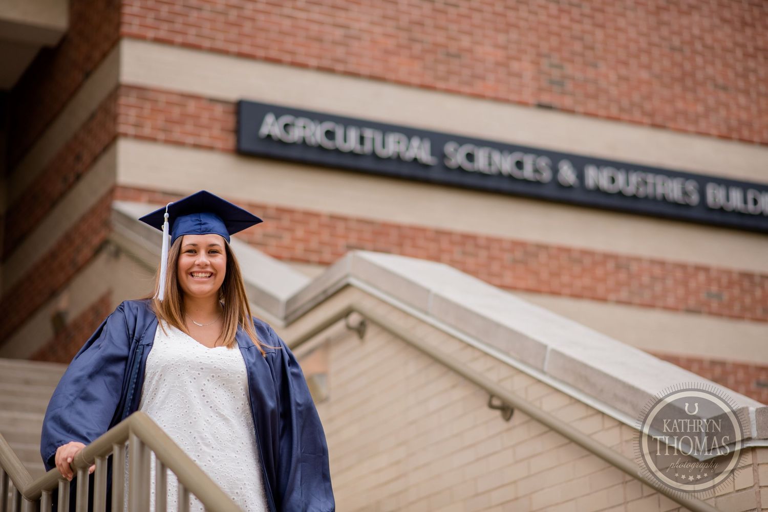 A graduate poses in front of the Agricultural Sciences building wearing traditional commencement attire.