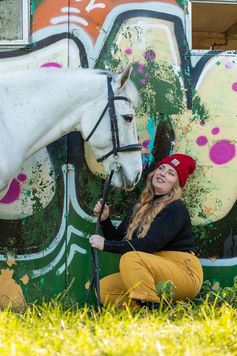 A playful outdoor scene with a white horse against vibrant graffiti art and yellow grass.