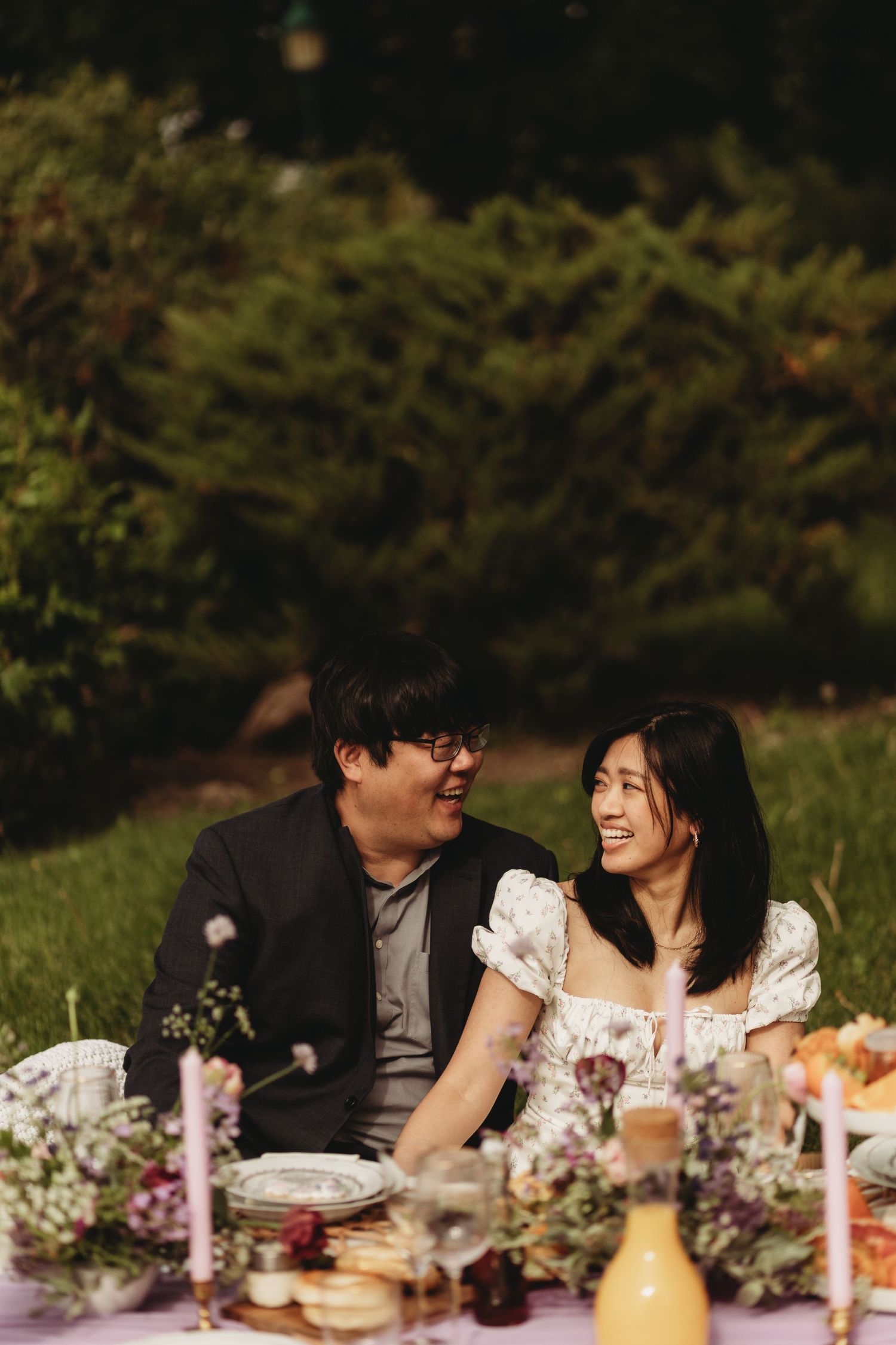 Couple sharing laughter at an outdoor dinner table decorated with flowers and candles.