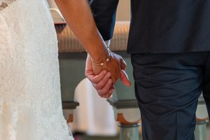 Close-up of bride and groom holding hands during wedding ceremony, bride in lace gown.