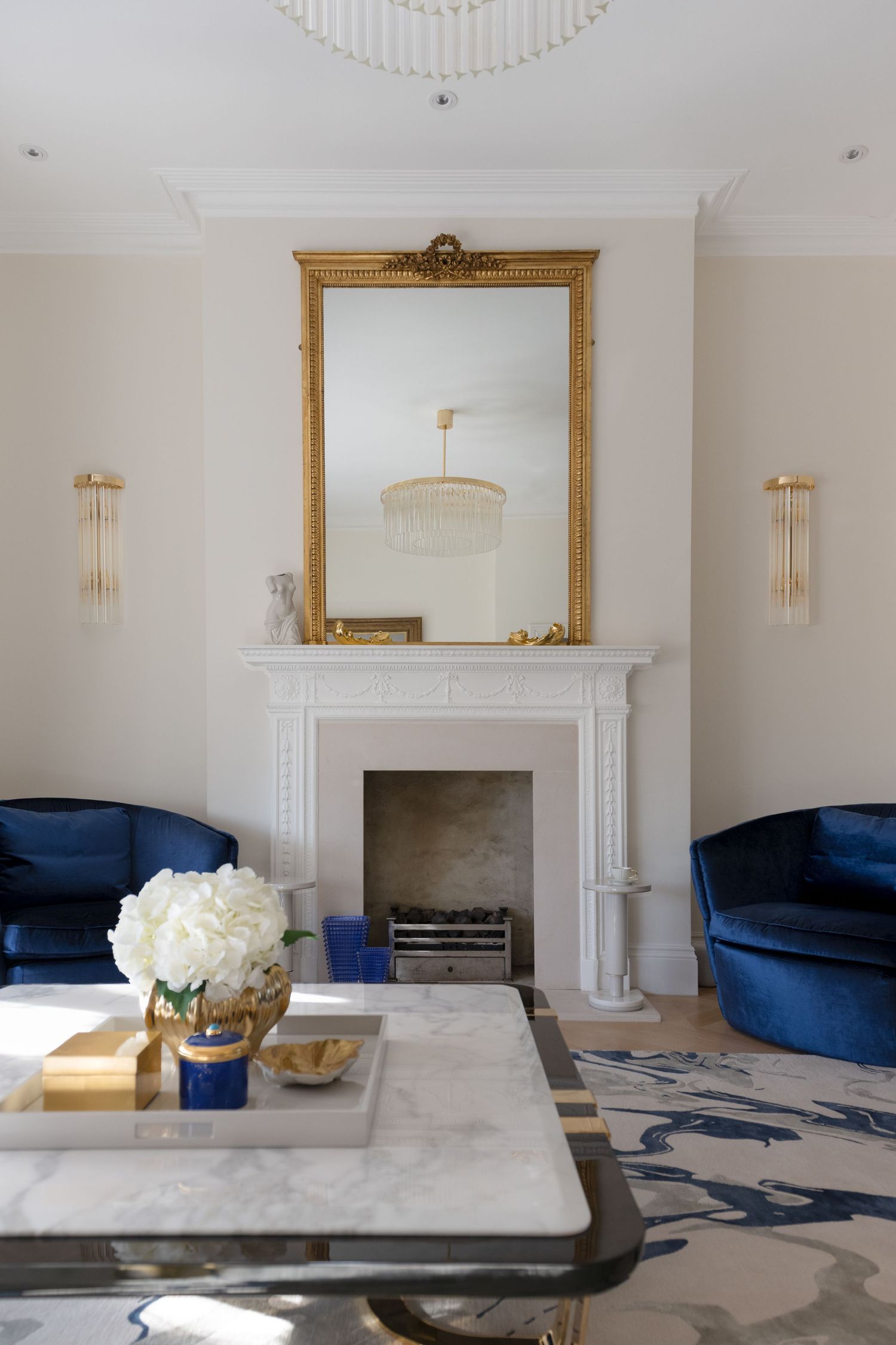Classic chimney with a gold mirror above where there is a reflection of a chandelier