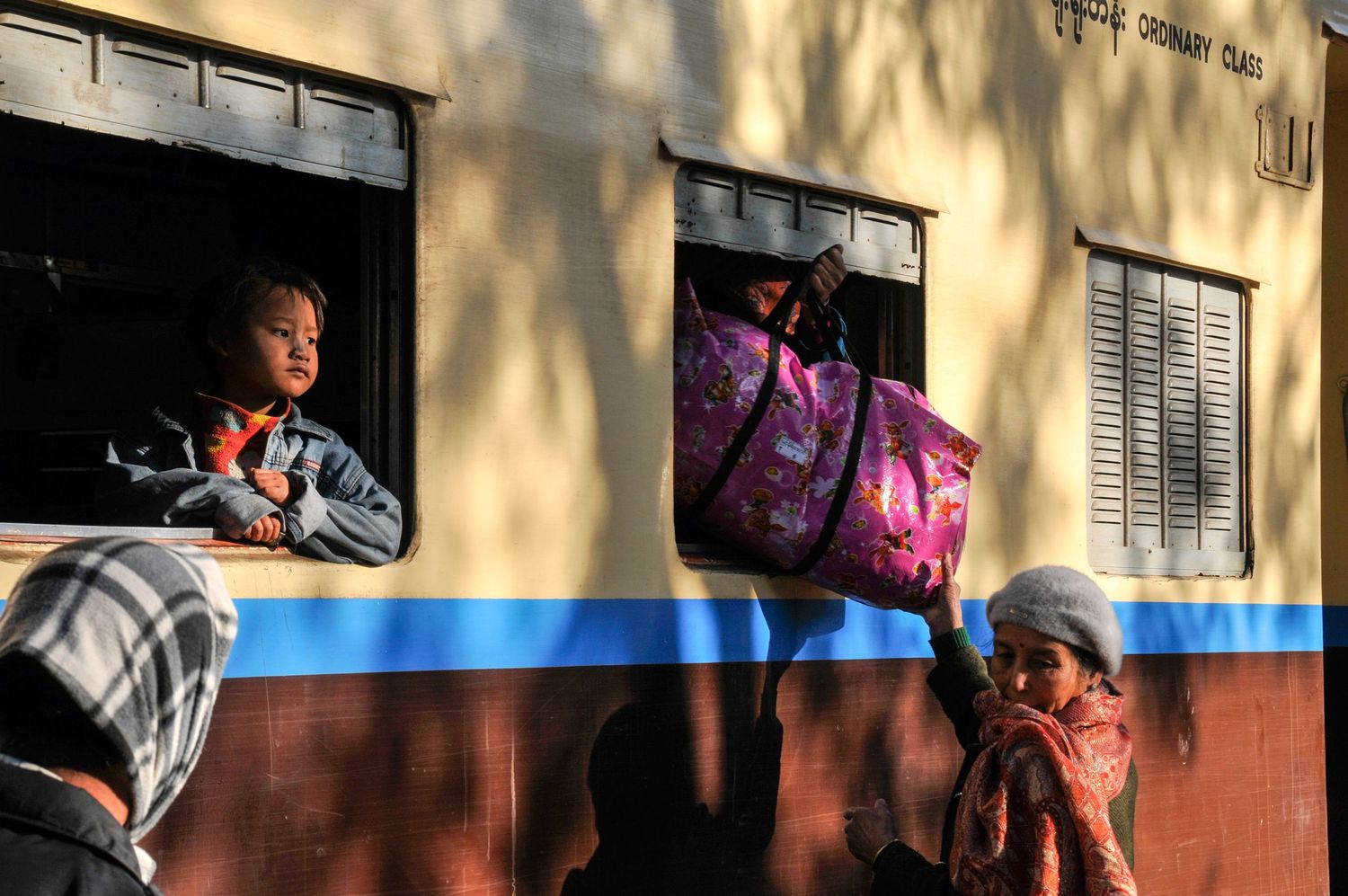 Girl stares dreamily out of train in Myanmar and through another window a bag is handed over