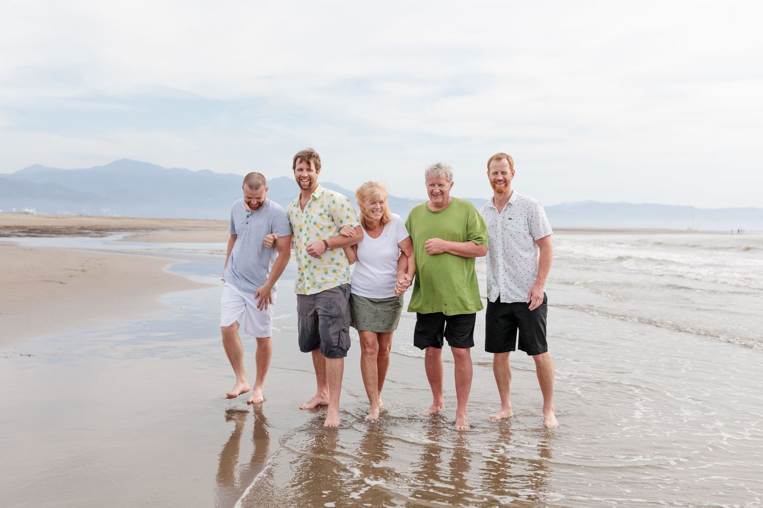 Group portrait of beachgoers standing together in the surf with mountains in the background.