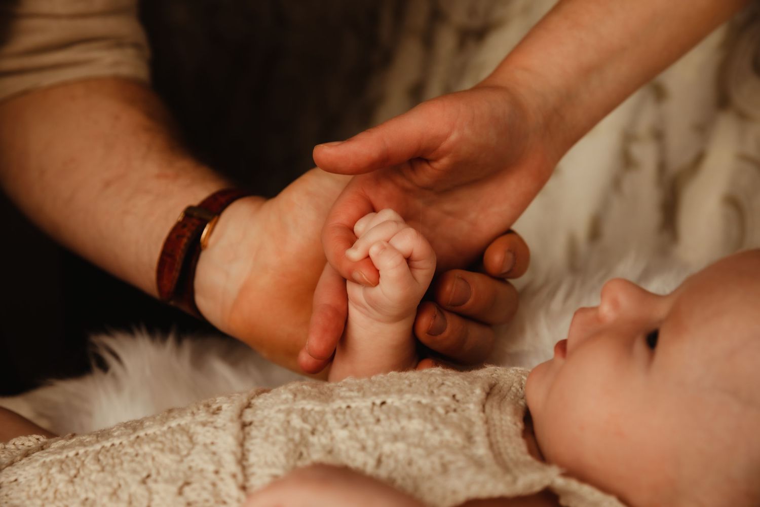 Newborn holding parents hands. Image by dmcgphoto