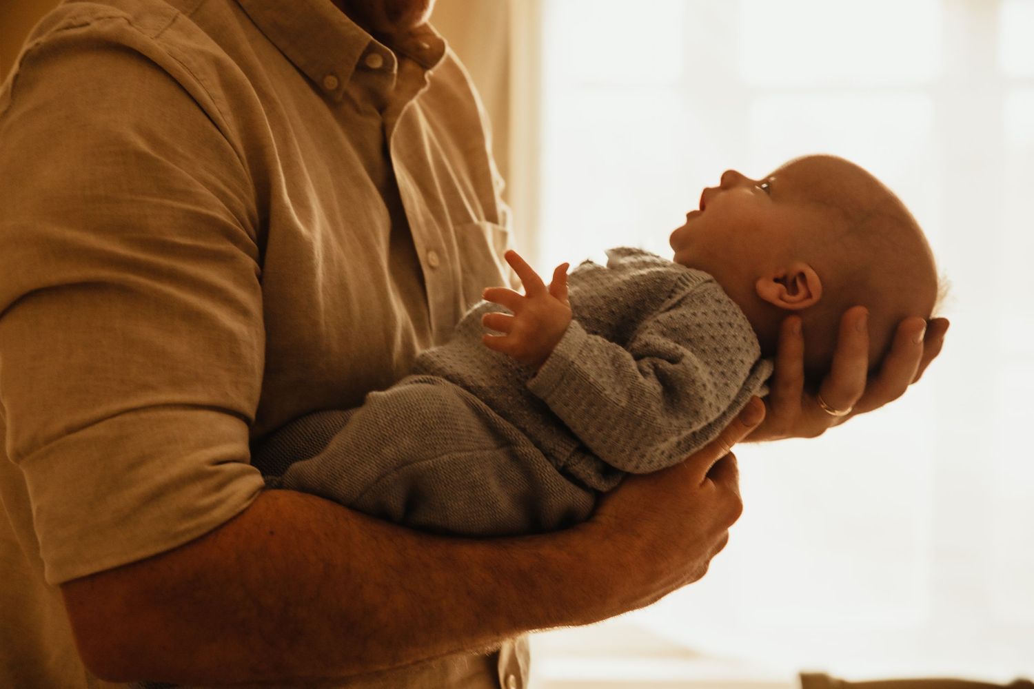 Newborn held in father's arms. Image by dmcgphoto