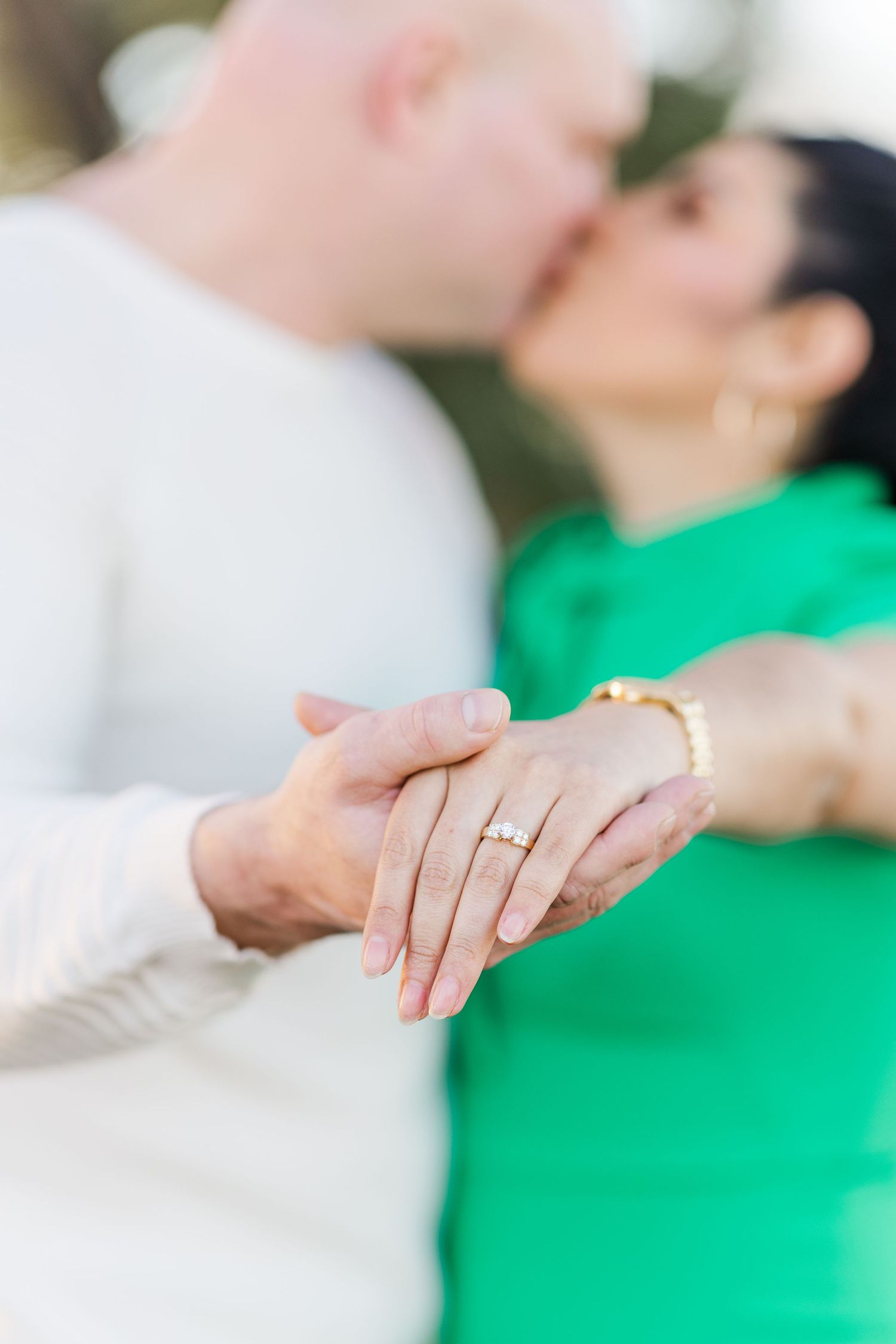 Hands intertwined showing off engagement ring against green background.