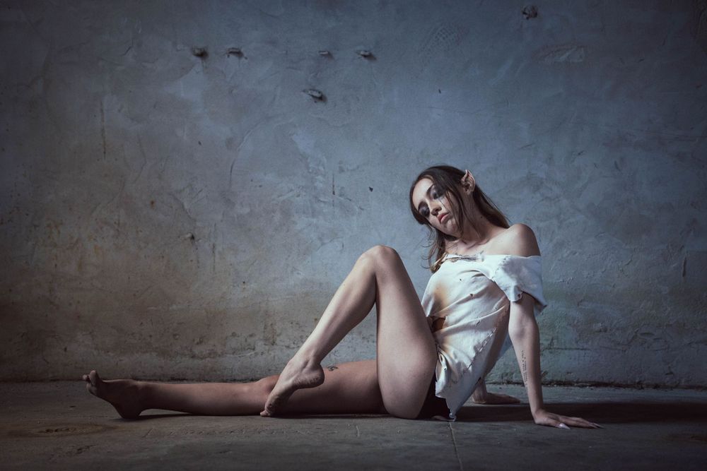 Artistic portrait of pointy ear model in white fabric against industrial concrete backdrop.