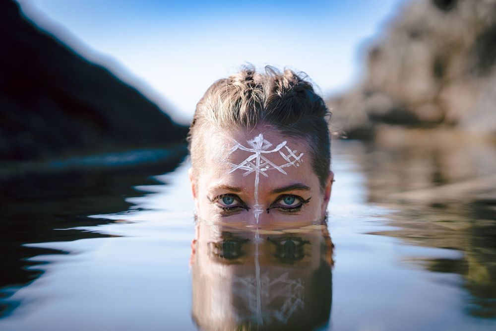 Mystical portrait showing face paint reflection in still waters.