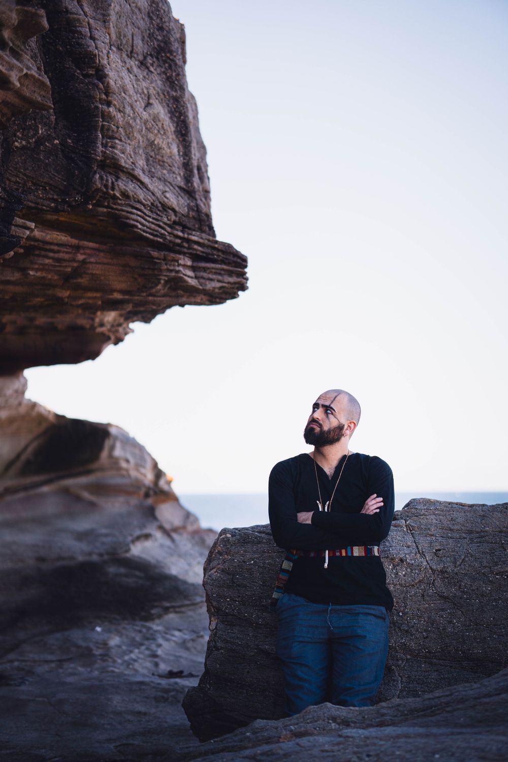 Person in black sweater stands against dramatic rocky cliff formation at sunset.