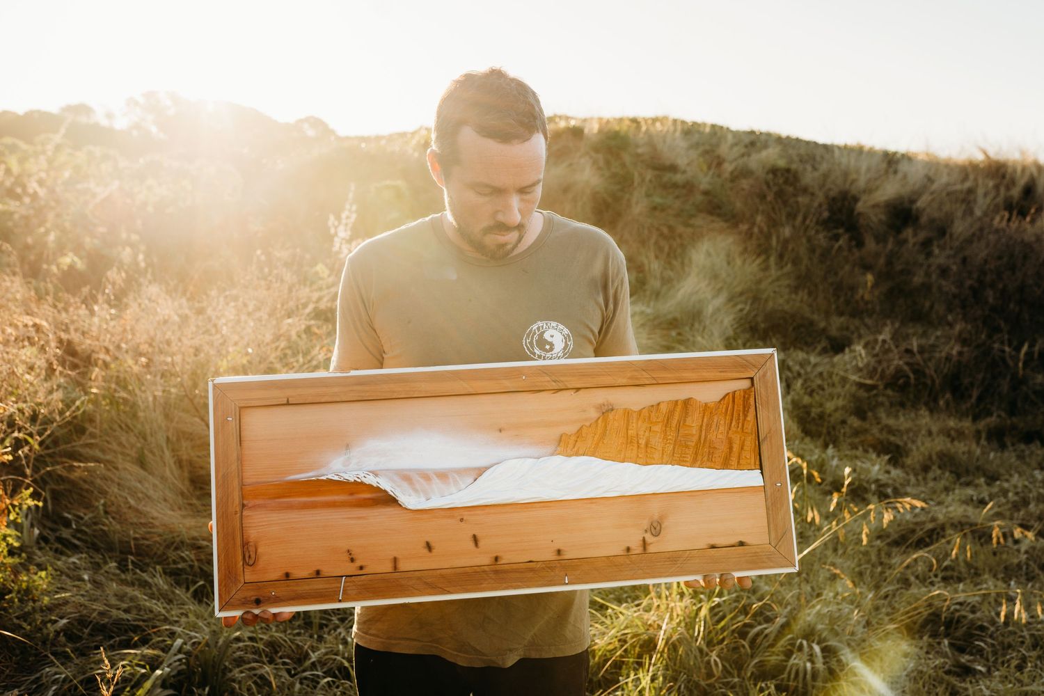 A person holding a wooden display case outdoors during golden hour.
