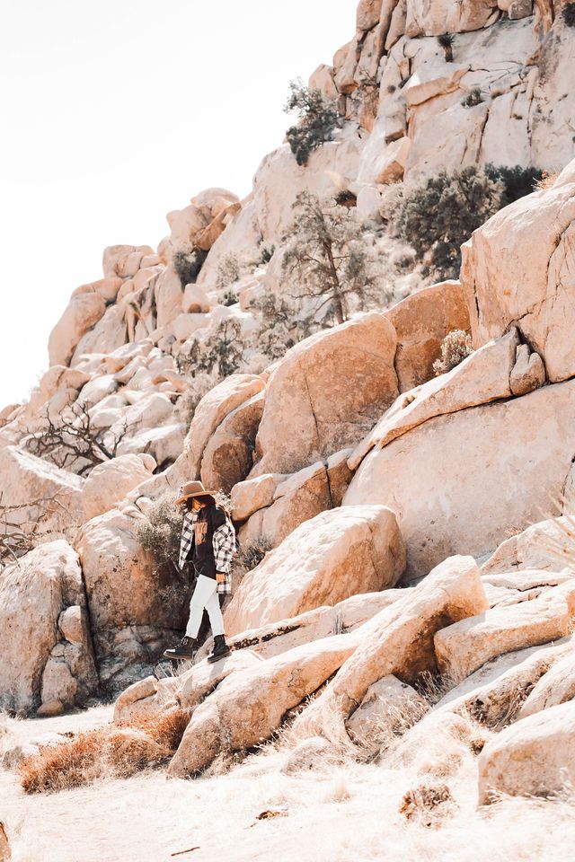 Person in leopard print exploring rocky desert terrain among large boulders.