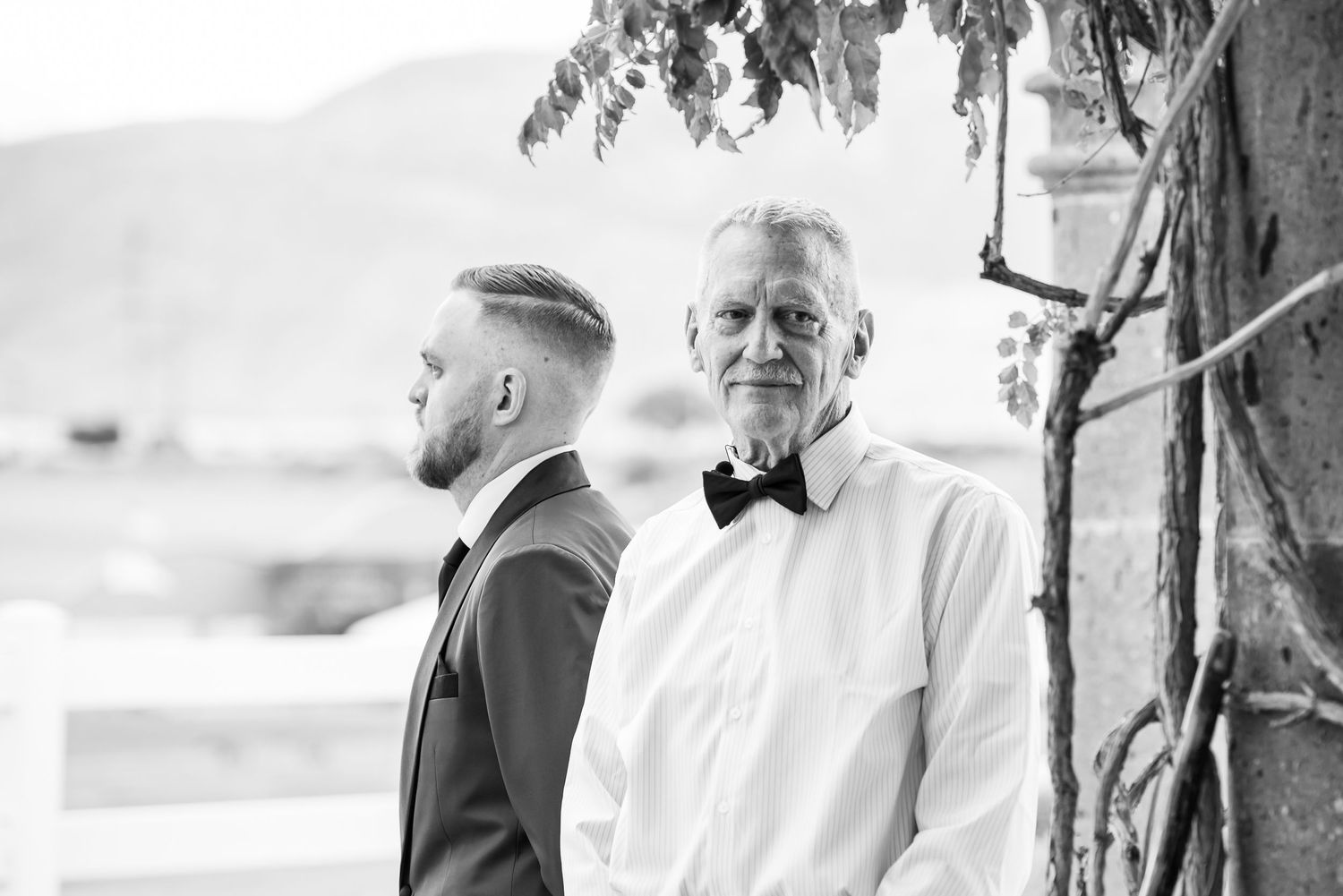 Black and white portrait of two men in formal attire standing outdoors.