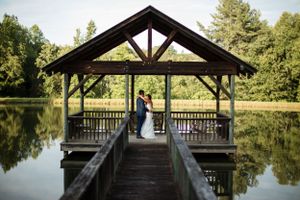 Rustic wooden pavilion overlooking a serene pond surrounded by trees.