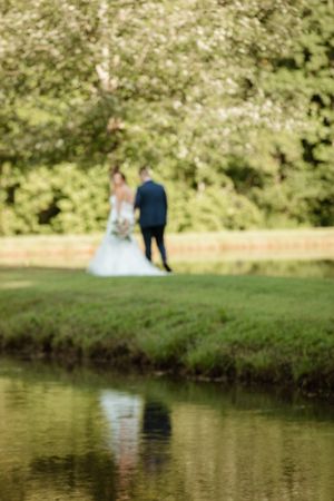 A dreamy out-of-focus shot of a couple by a pond reflects their silhouettes in the water.