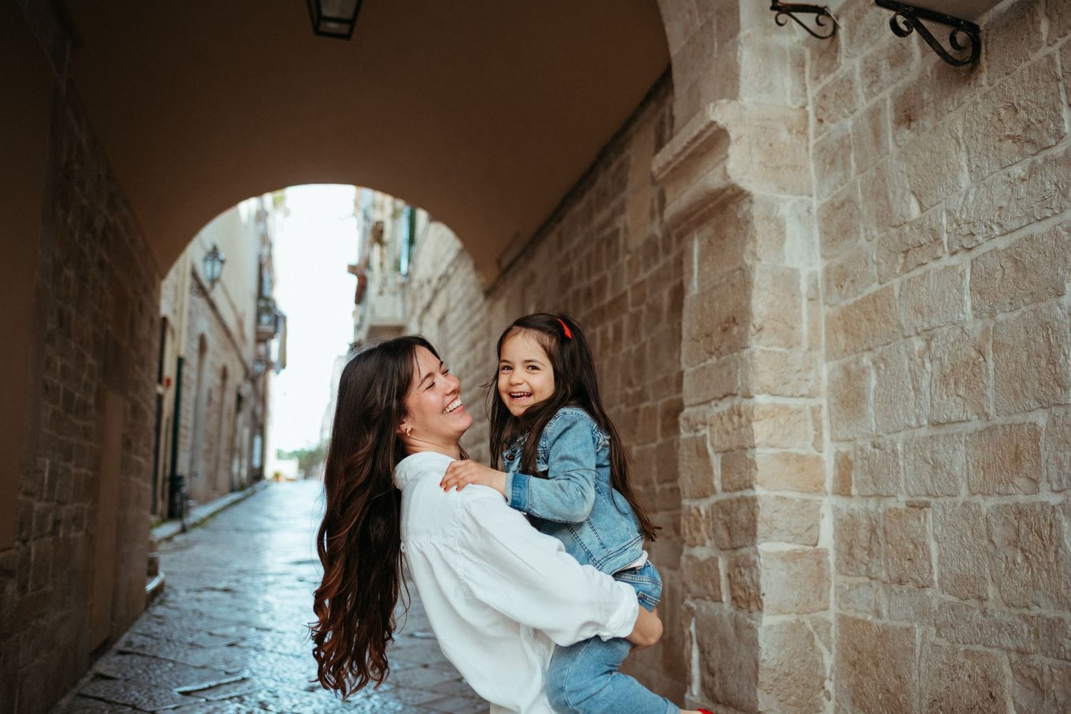 Two people sharing joyful moment in narrow stone alleyway with arched architecture.