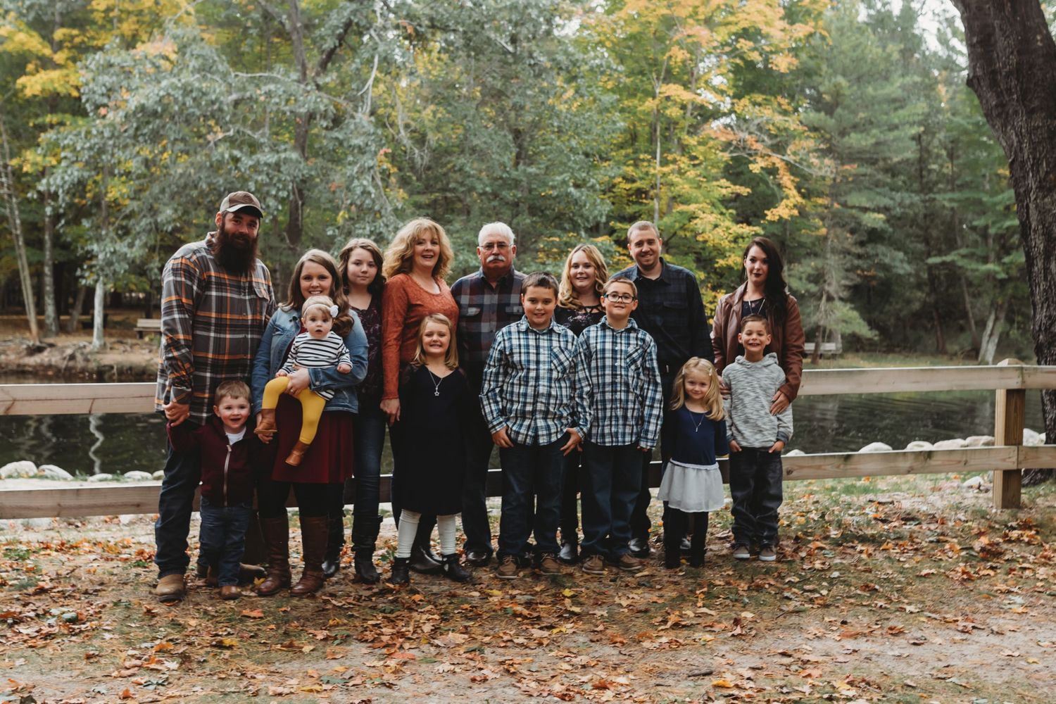 A large group poses for a family photo outdoors near a lake on an autumn day.